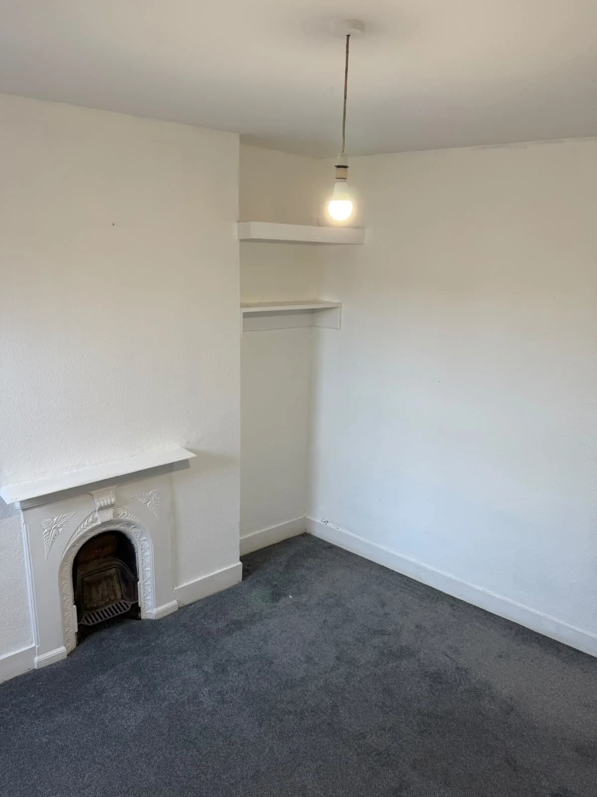 Existing bedroom at Lancaster Road with small arched fireplace and dark carpet, before renovation